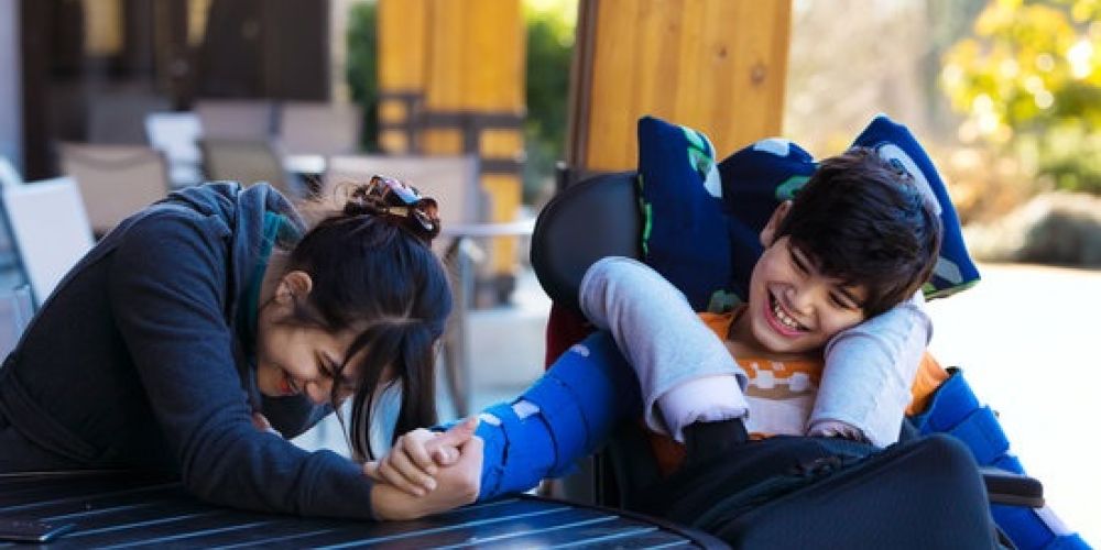 Disabled boy in wheelchair arm wrestling with caregiver outdoors
