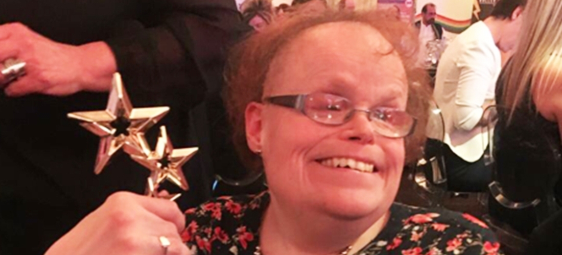Images shows Lou Townsend smiling at the camera and holding up her Positive Role Model Award, the award is two gold stars connected to each other one bigger than the other.