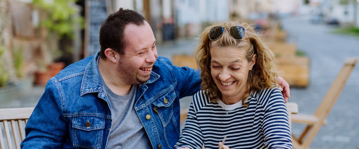 A couple sitting at an outdoor table looking at a cell phone.