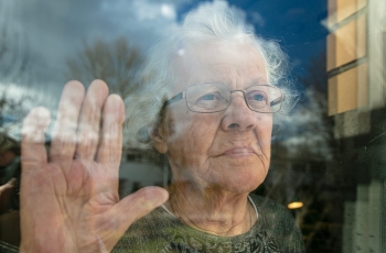 Independent Mental Capacity Advocacy. Elderly lady holding her hand up to the glass staring out.