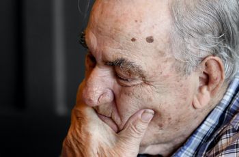 An old gentleman sat with his hand covering the bottom part of his face, he looks worried.