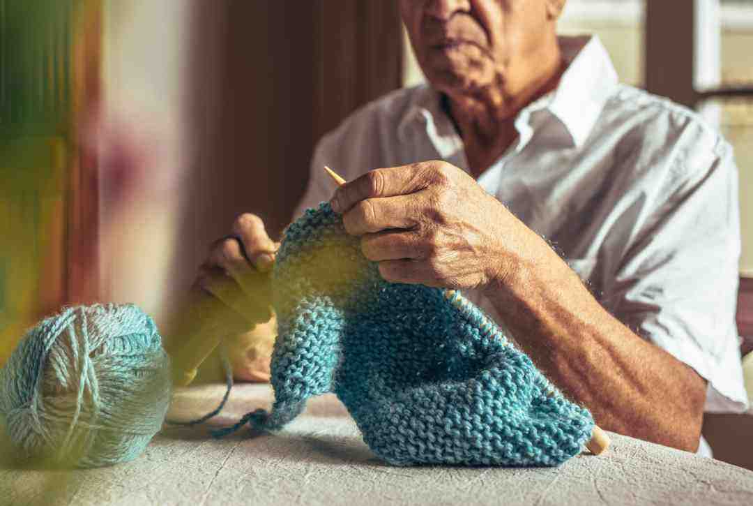 Image of an older gentlemen knitting with green yarn